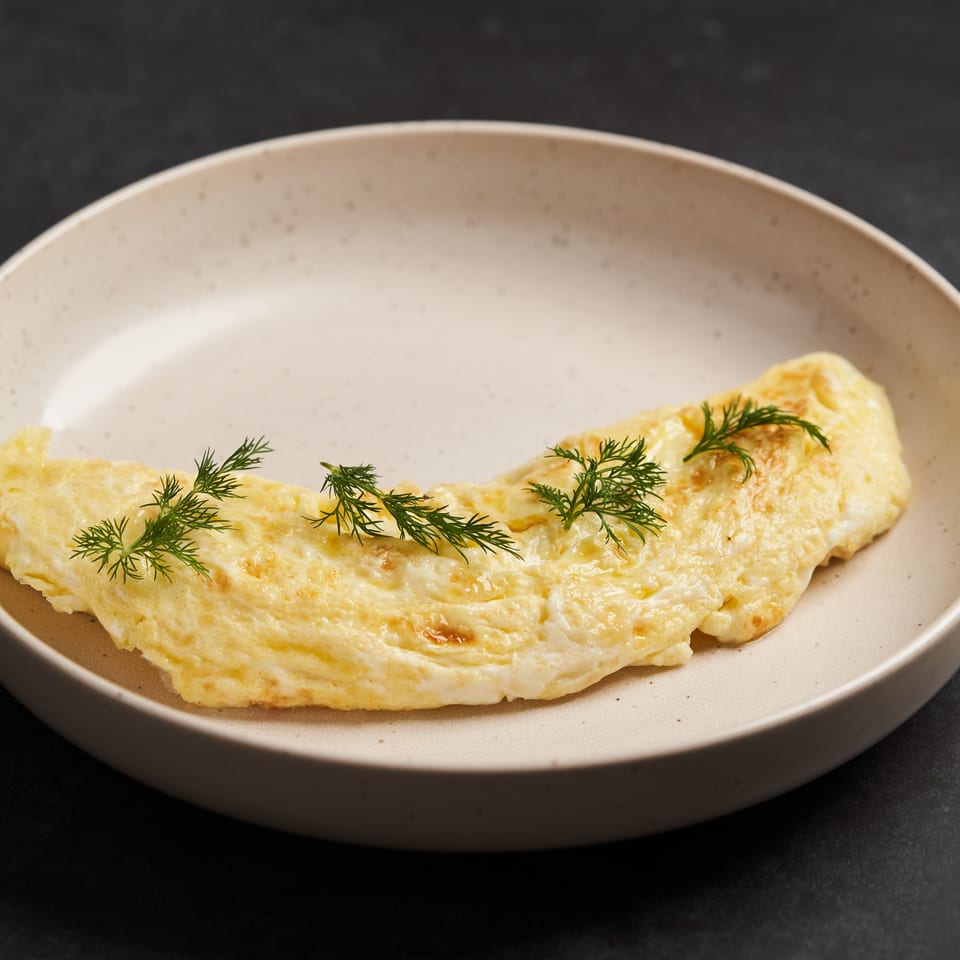 A fluffy yellow omelet garnished with fresh dill sprigs, served on a light speckled plate.
