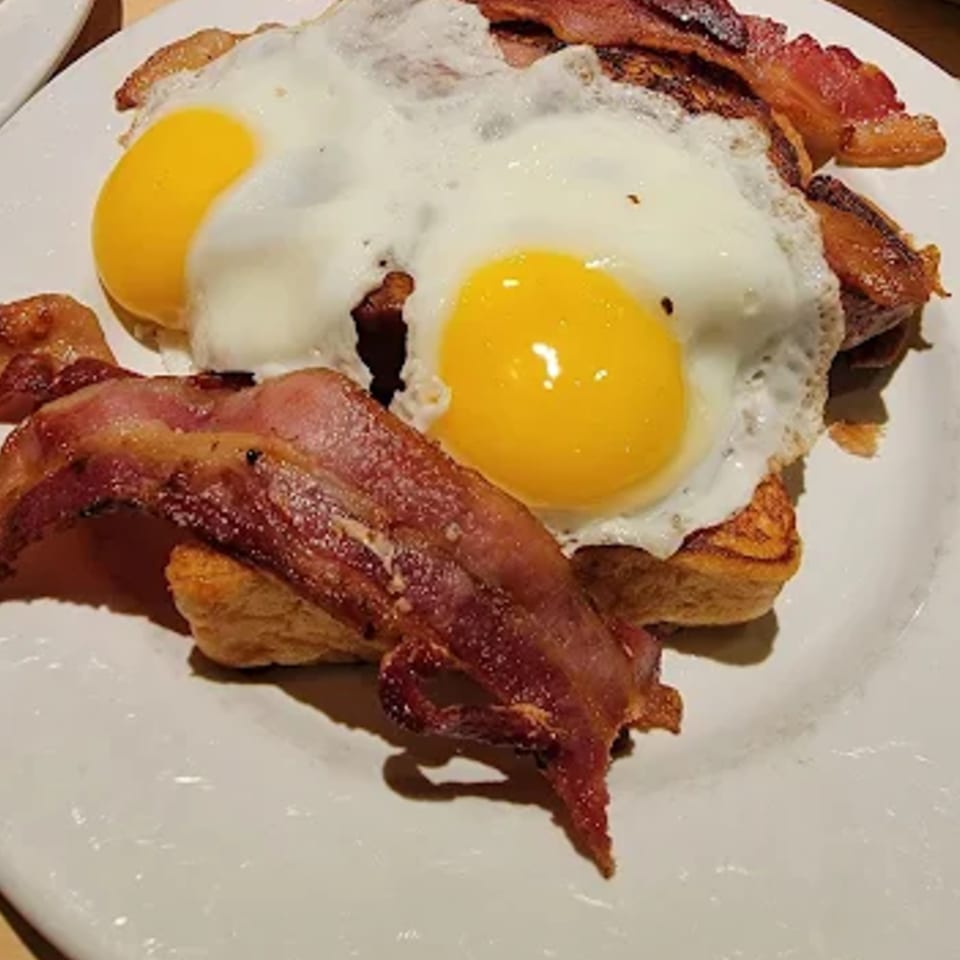 Two sunny-side-up eggs and crispy bacon strips on a plate, a classic diner breakfast.
