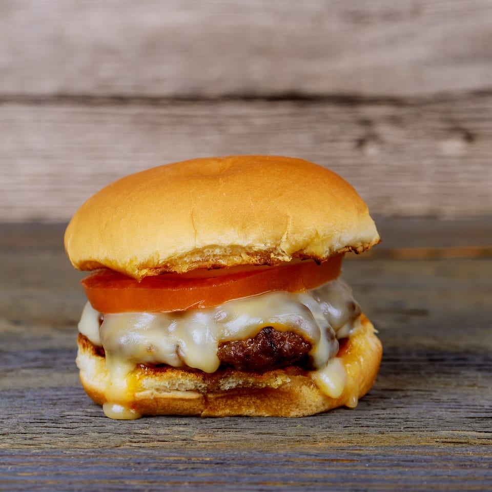 A cheesy Orion Diner burger with melted white cheese and a tomato slice on a wooden surface.