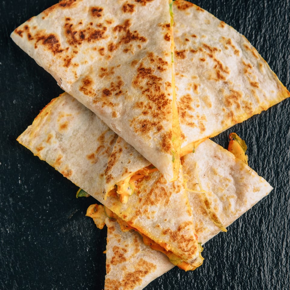 Three golden-brown quesadilla wedges with melted cheese and green peppers, on a dark textured surface.